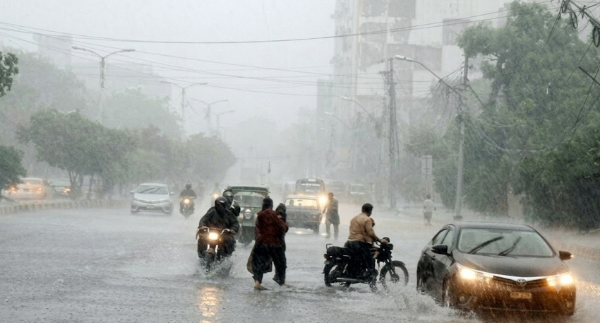 Heavy rain floods a busy Pakistan street with cars and motorbikes splashing through deep water.
