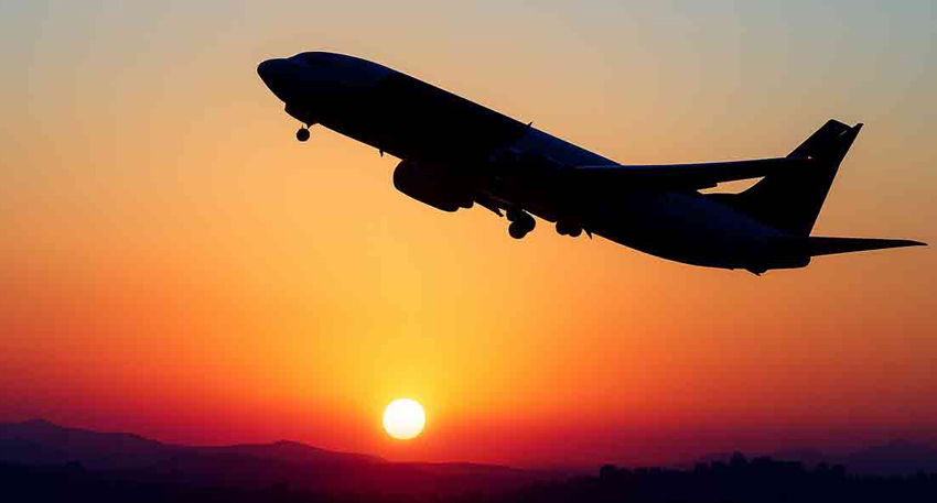 Silhouette of a jet aircraft taking off into a vibrant orange sunrise over a mountainous horizon.