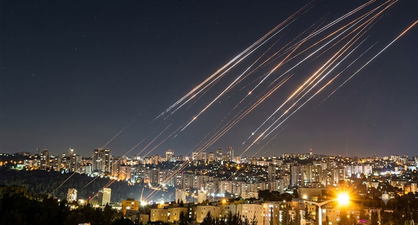 Night city skyline with multiple bright streaks from missile interceptions illuminating the dark sky.