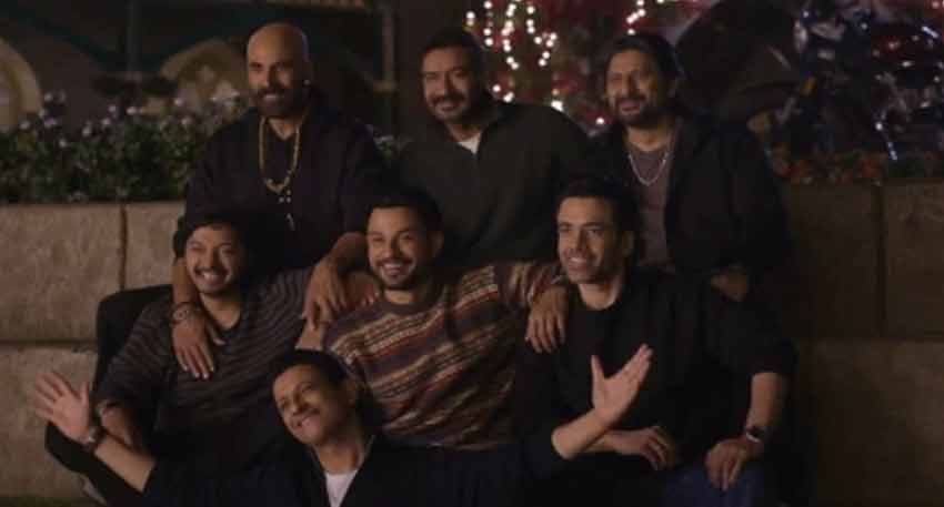 Seven men, including Ajay Devgn, smiling and posing together for a group photo outdoors at night.