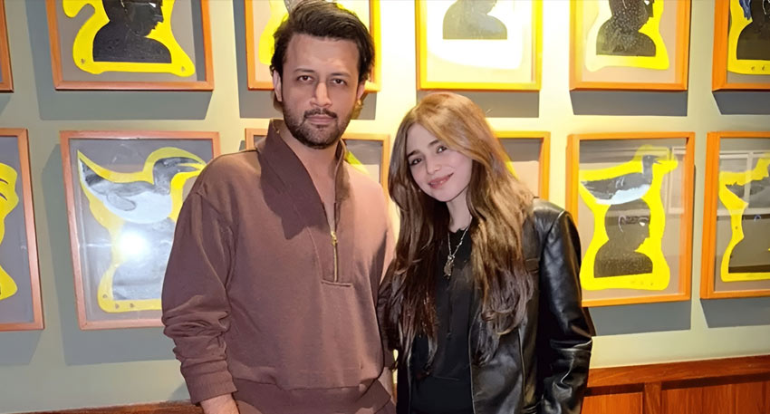 Atif Aslam and Aima Baig posing in front of yellow-framed artwork.