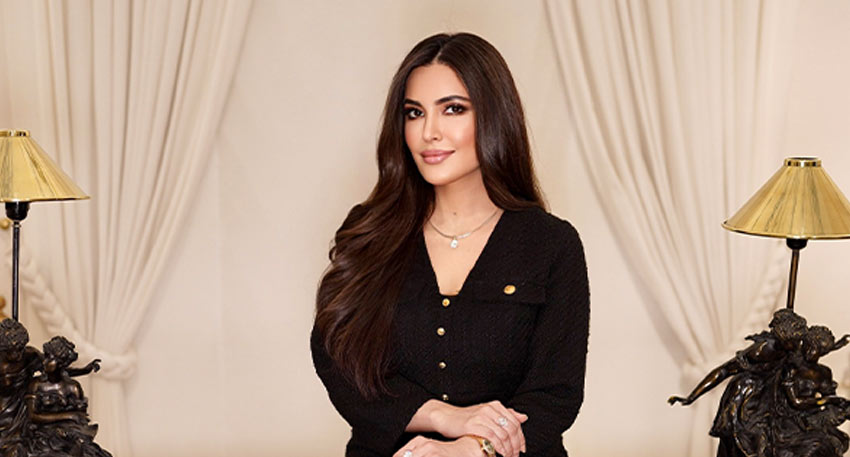 Dr. Fazeela Abbasi posing in a black dress between two gold lamps.