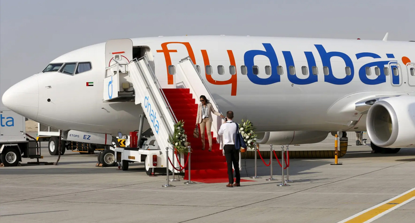 A white flydubai Boeing 737 aircraft on an airport tarmac with passengers on red-carpeted stairs.