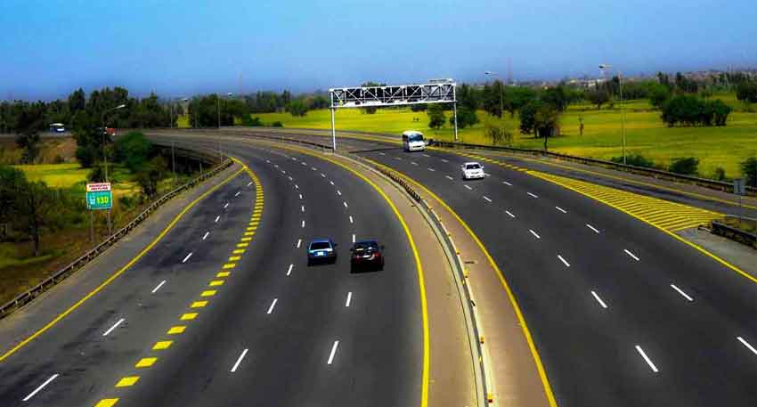 Wide view of a multi-lane motorway in Pakistan with cars driving past green fields and road signs.