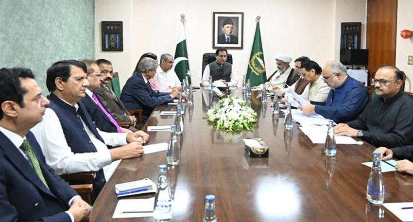Pakistani officials hold a high-level government and opposition meeting around a large wooden conference table.