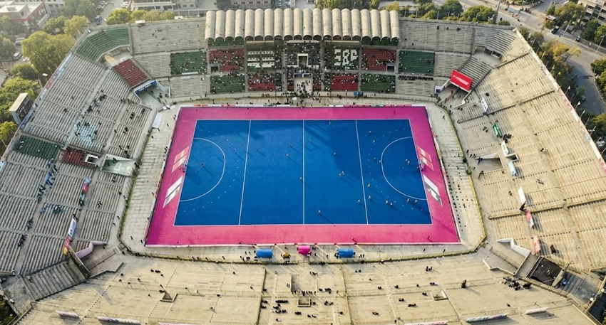 Aerial view of Lahore's National Hockey Stadium featuring its bright blue pitch and surrounding concrete stands.