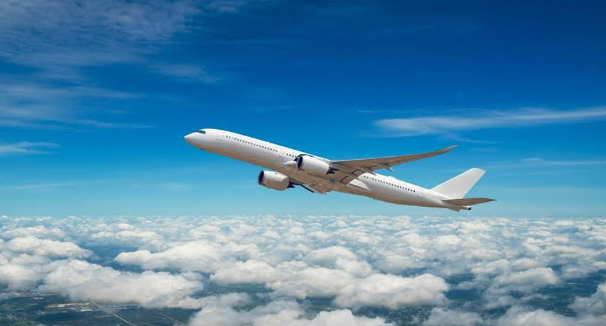 White passenger airplane flying high above white clouds under a clear blue sky.