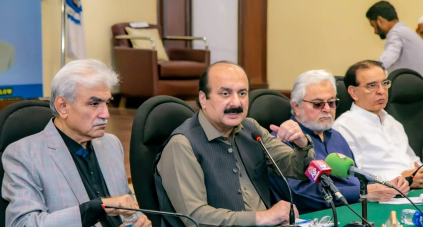 Pakistani officials holding a press conference with microphones on a green table.