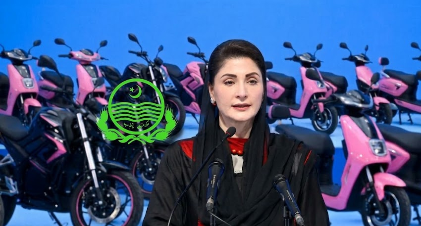 Maryam Nawaz speaking at a podium with rows of pink and black electric bikes in the background.