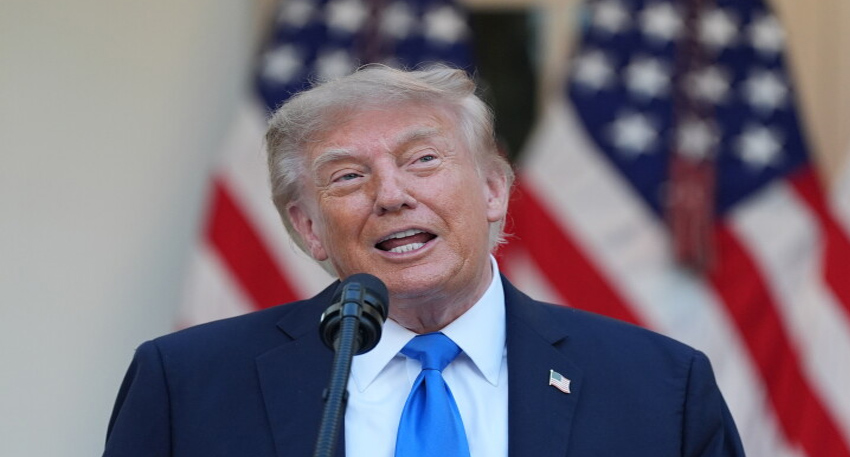 Donald Trump at a microphone with American flags in the background.