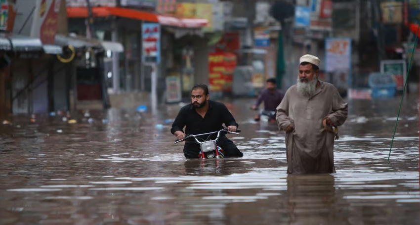Men navigate a heavily flooded city street on foot and by motorcycle during heavy rainfall.