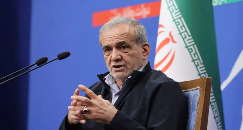 Iranian President Masoud Pezeshkian speaking behind microphones with Iran's flag behind him.