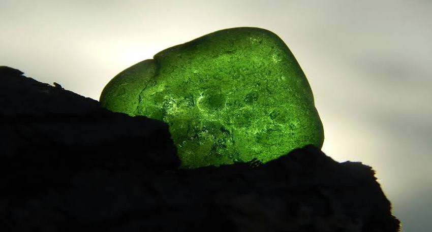 Glowing green uranium rock backlit against a cloudy sky.