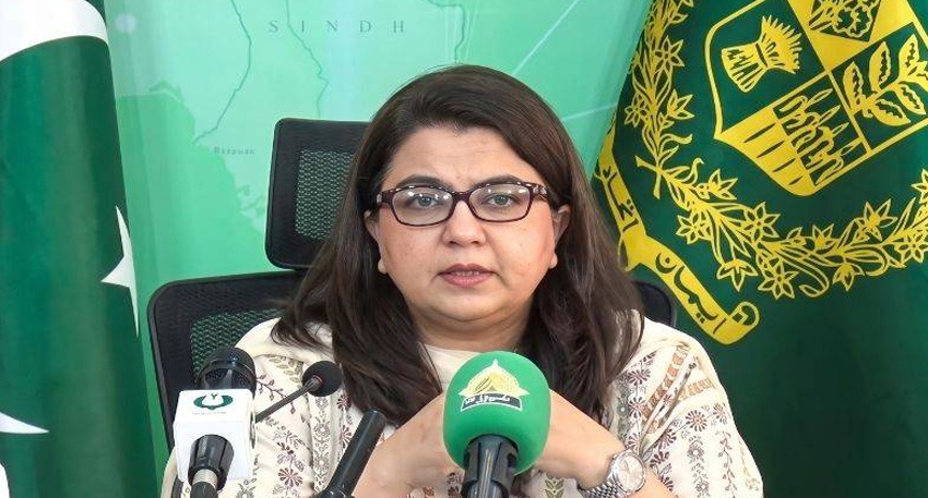 Shaza Fatima Khawaja speaking at a press conference in front of Pakistani flags.