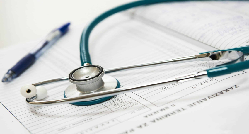 Stethoscope resting on medical paperwork next to a blue pen.