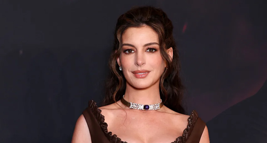 Anne Hathaway at a red carpet event wearing a brown ruffled dress and a jeweled choker necklace.